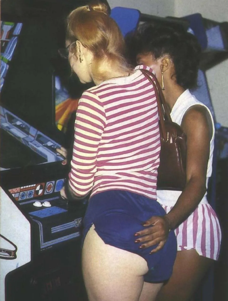 a pair of women at an arcade, with one's hand on the other's ass.