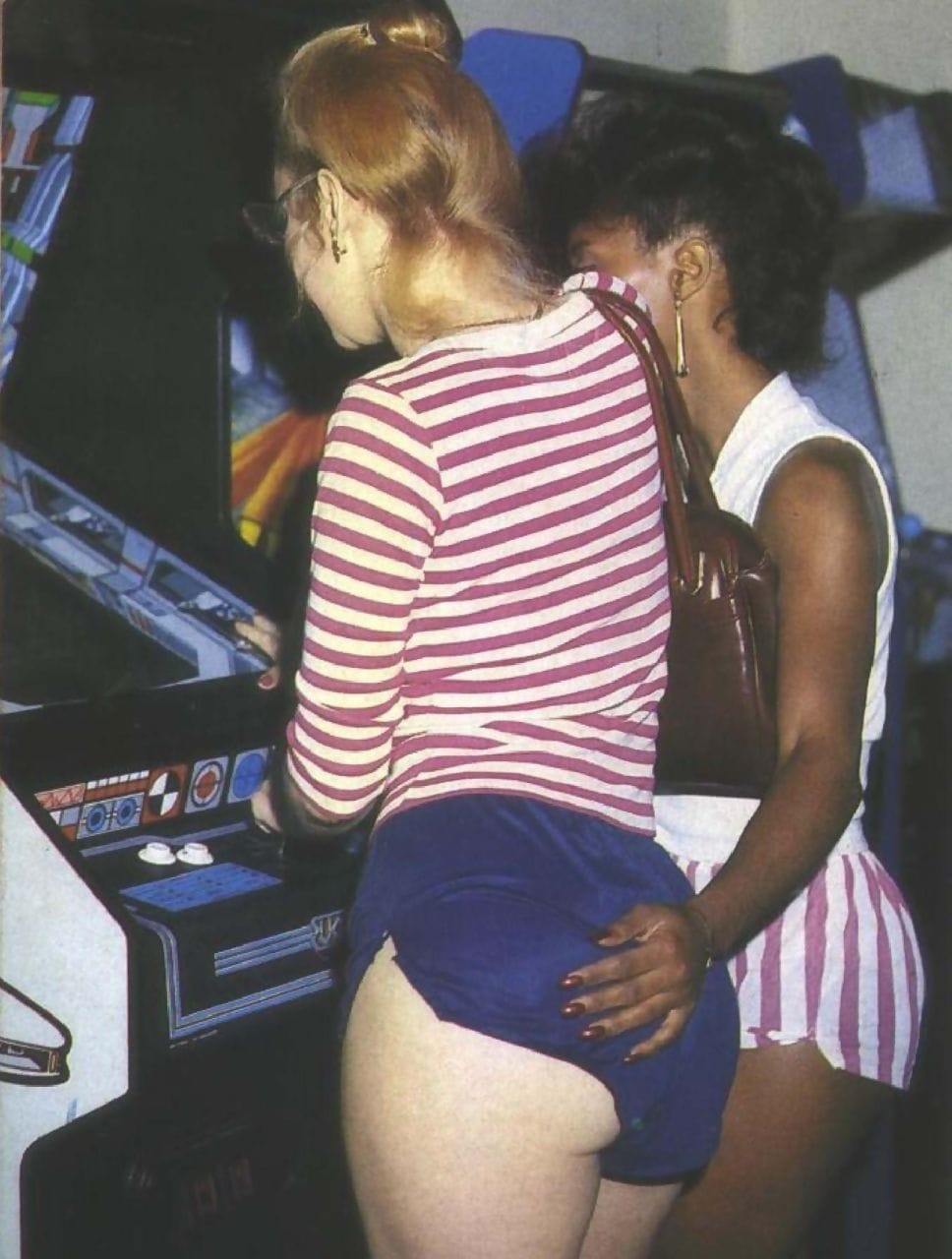 a pair of women at an arcade, with one's hand on the other's ass. 