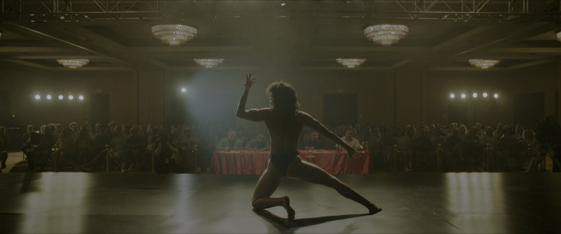 a muscular woman in a bikini poses in front of a room of onlookers